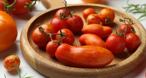 Different ripe tomatoes on white wooden table, closeup