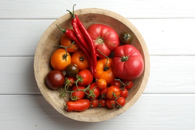 Photo of Different ripe tomatoes and chili peppers in bowl on white wooden table, top view