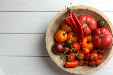 Photo of Different ripe tomatoes and chili peppers in bowl on white wooden table, top view. Space for text