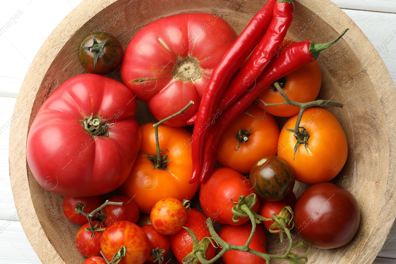 Photo of Different ripe tomatoes and chili peppers in bowl on white table, flat lay