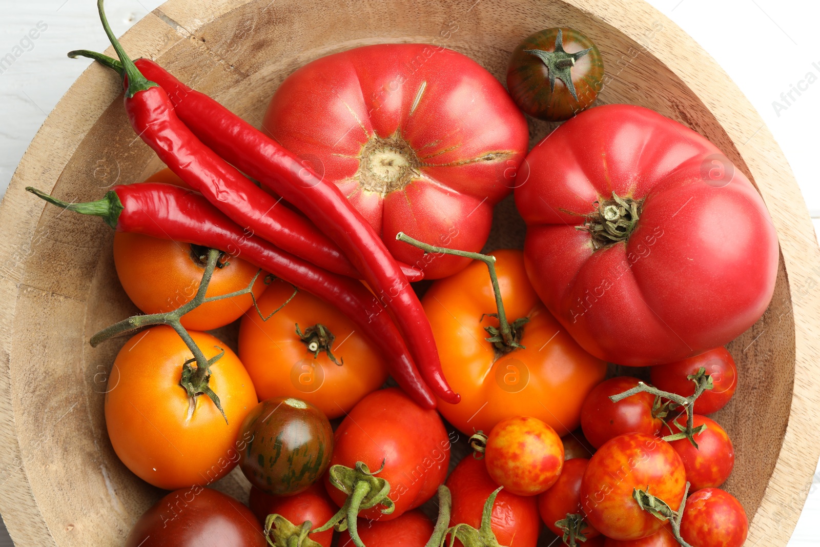 Photo of Different ripe tomatoes and chili peppers in bowl on white table, flat lay