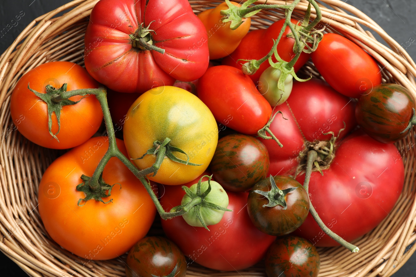 Photo of Different ripe and unripe tomatoes in wicker basket on table, top view