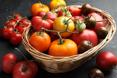 Basket with different ripe and unripe tomatoes on grey textured table, closeup