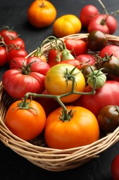 Photo of Different ripe and unripe tomatoes in wicker basket on grey table, closeup