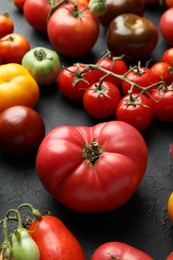 Photo of Different fresh tomatoes on grey textured table, closeup