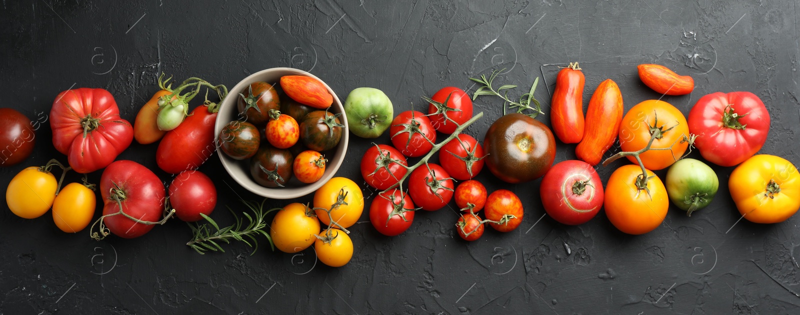 Photo of Different fresh tomatoes and rosemary on grey textured table, flat lay