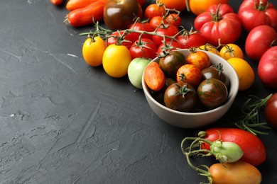 Photo of Different fresh tomatoes on grey textured table. Space for text