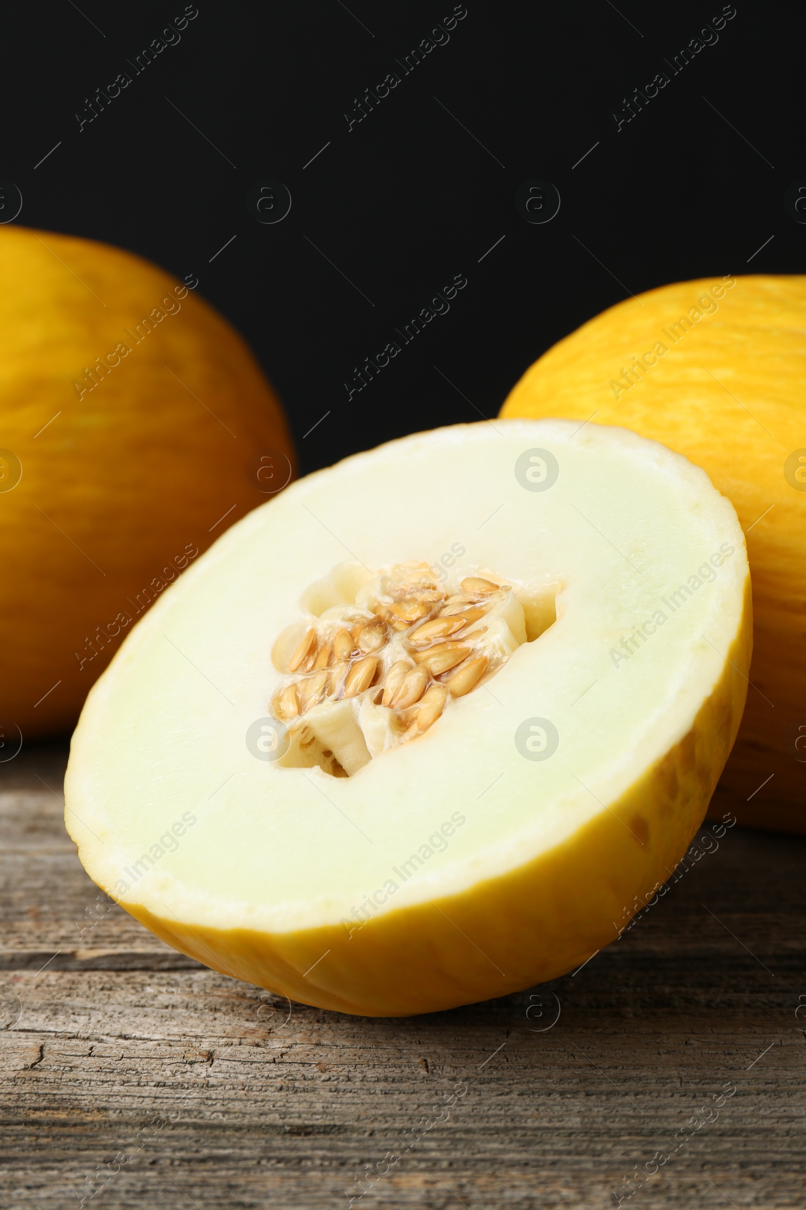 Photo of Fresh ripe melons on wooden table against black background, closeup