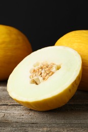 Photo of Fresh ripe melons on wooden table against black background, closeup