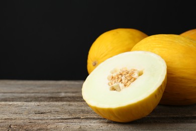 Photo of Fresh ripe melons on wooden table against black background, space for text