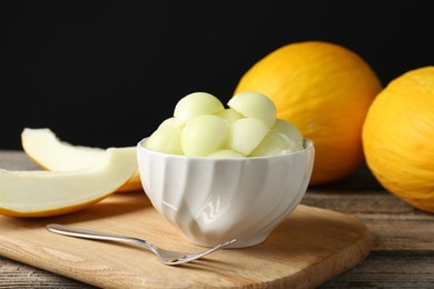 Photo of Melon balls in bowl and fresh fruits on wooden table against black background