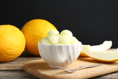 Photo of Melon balls in bowl and fresh fruits on wooden table against black background