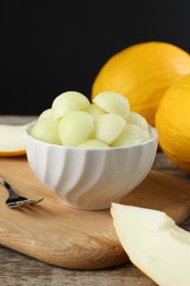 Melon balls in bowl and fresh fruits on wooden table against black background, closeup