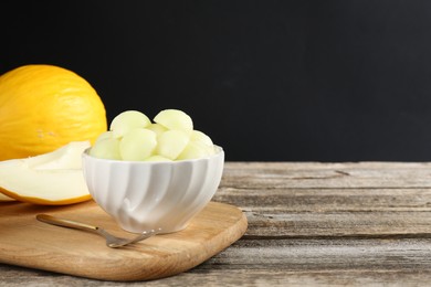 Photo of Melon balls in bowl and fresh fruits on wooden table against black background, space for text