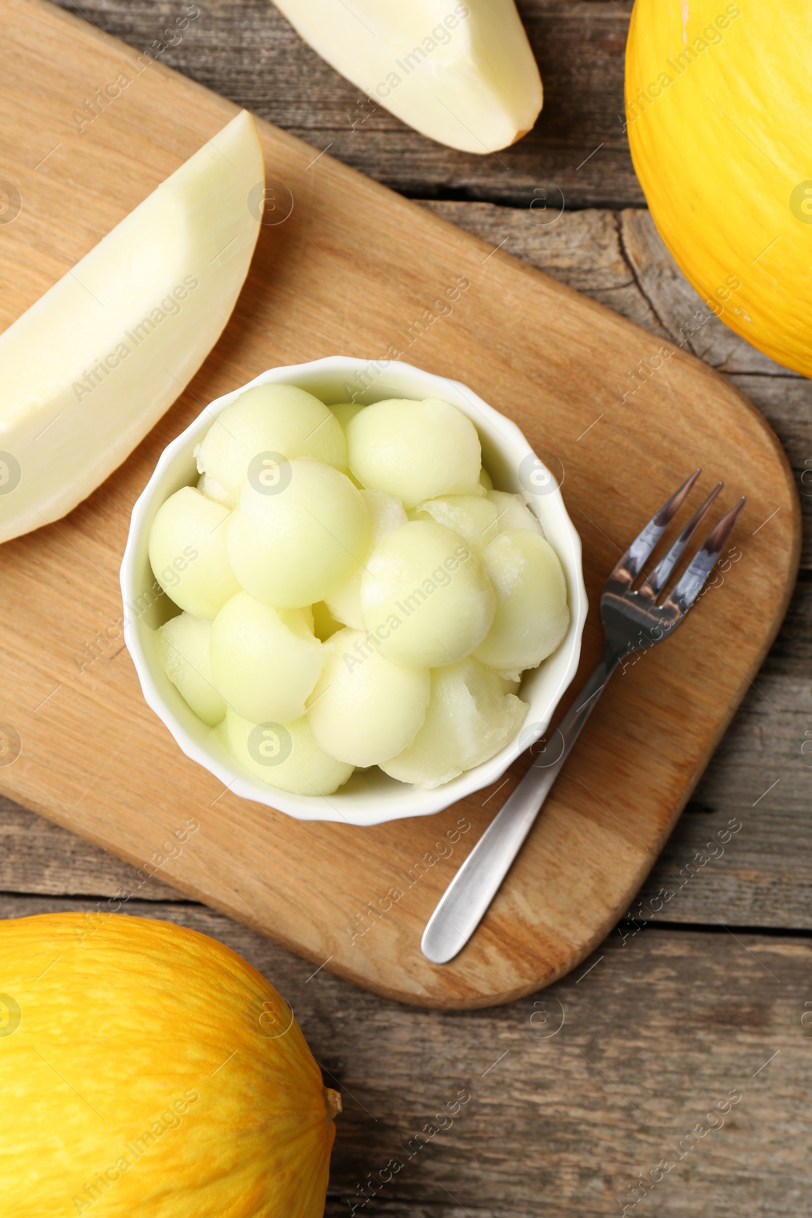 Photo of Melon balls in bowl and fresh fruits on wooden table, flat lay