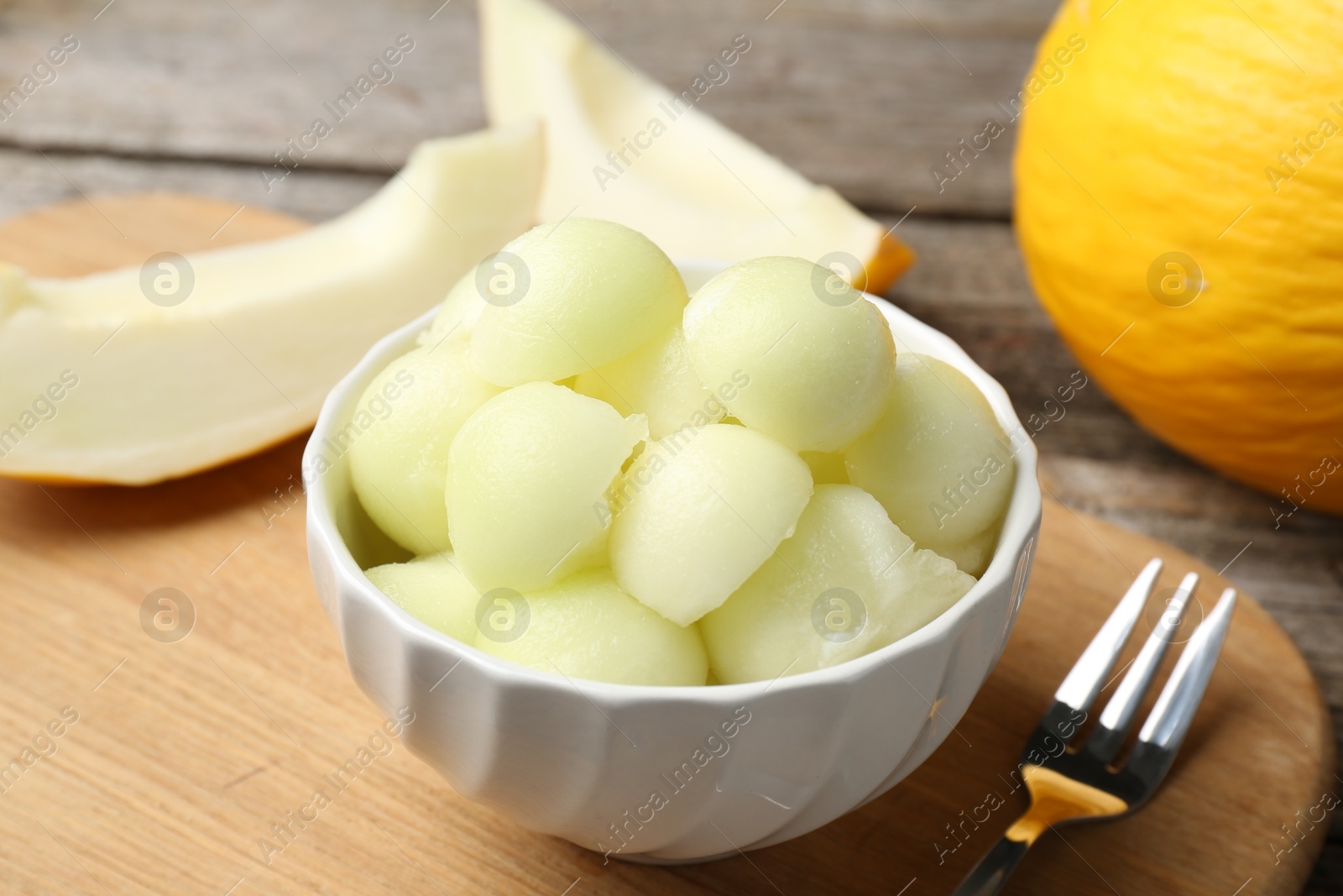 Photo of Melon balls in bowl and fresh fruits on wooden table, closeup