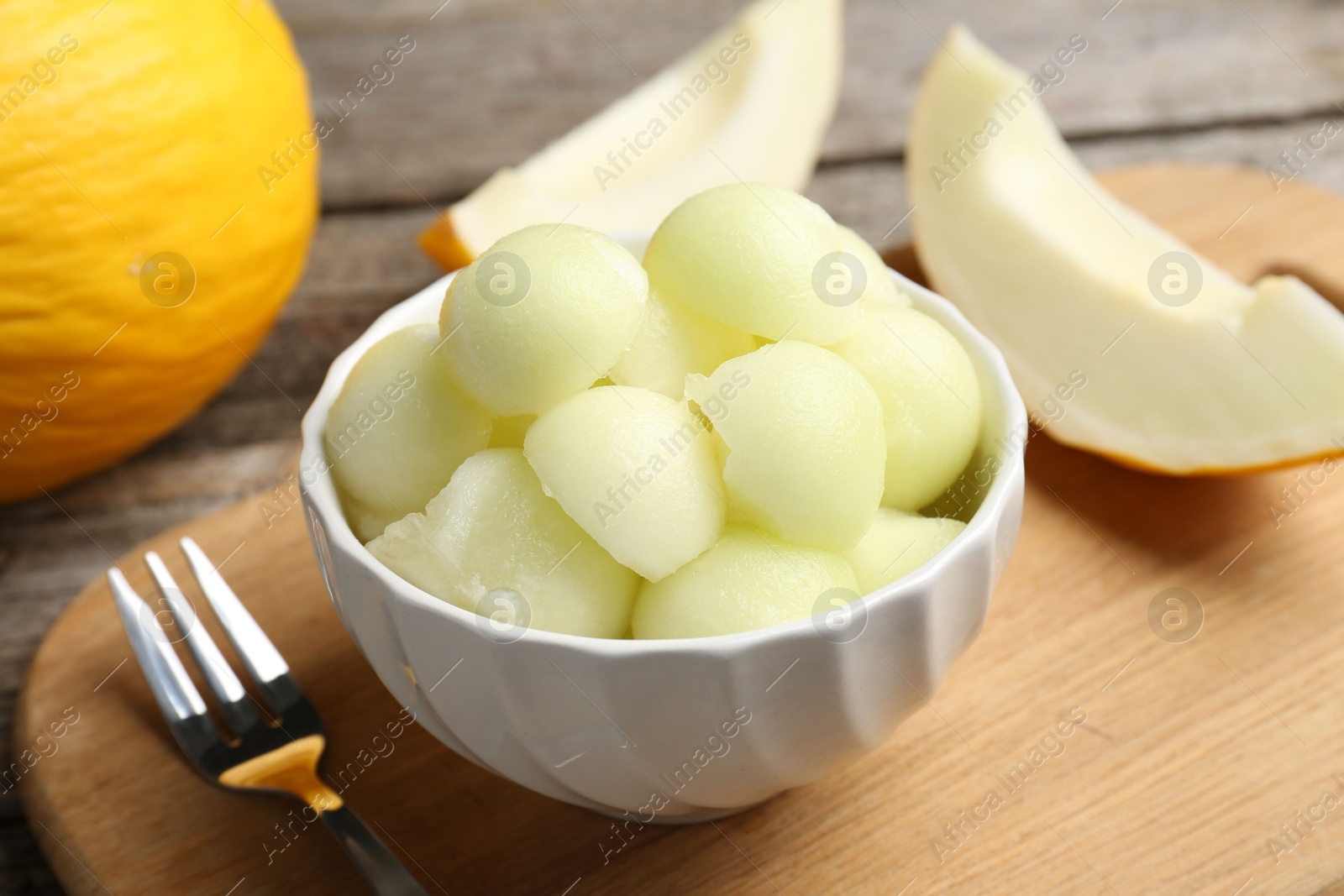 Photo of Melon balls in bowl and fresh fruits on wooden table, closeup