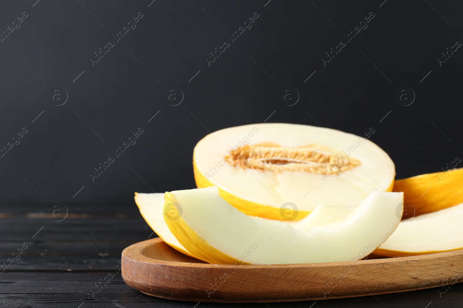 Photo of Fresh ripe melons on wooden table against black background, space for text