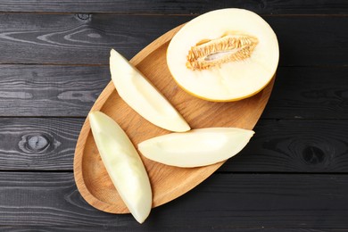 Cut fresh ripe melon on black wooden table, top view