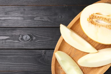 Photo of Cut fresh ripe melon on black wooden table, top view. Space for text