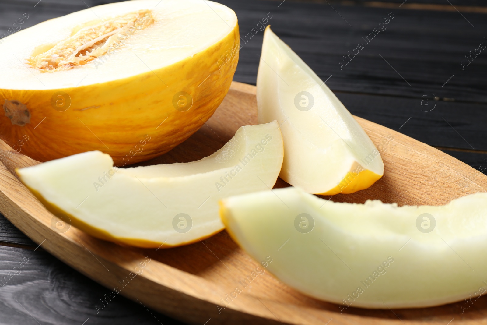 Photo of Cut fresh ripe melon on black wooden table, closeup