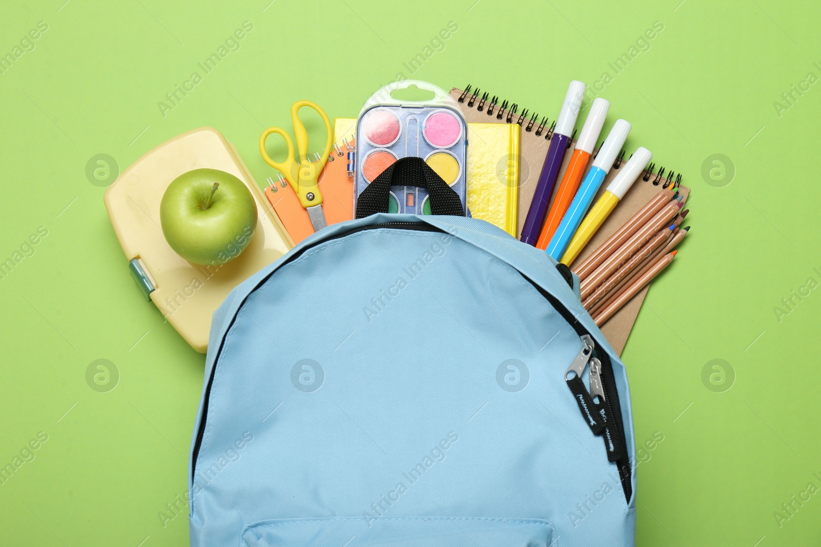 Photo of Light blue school backpack with stationery on green background, top view