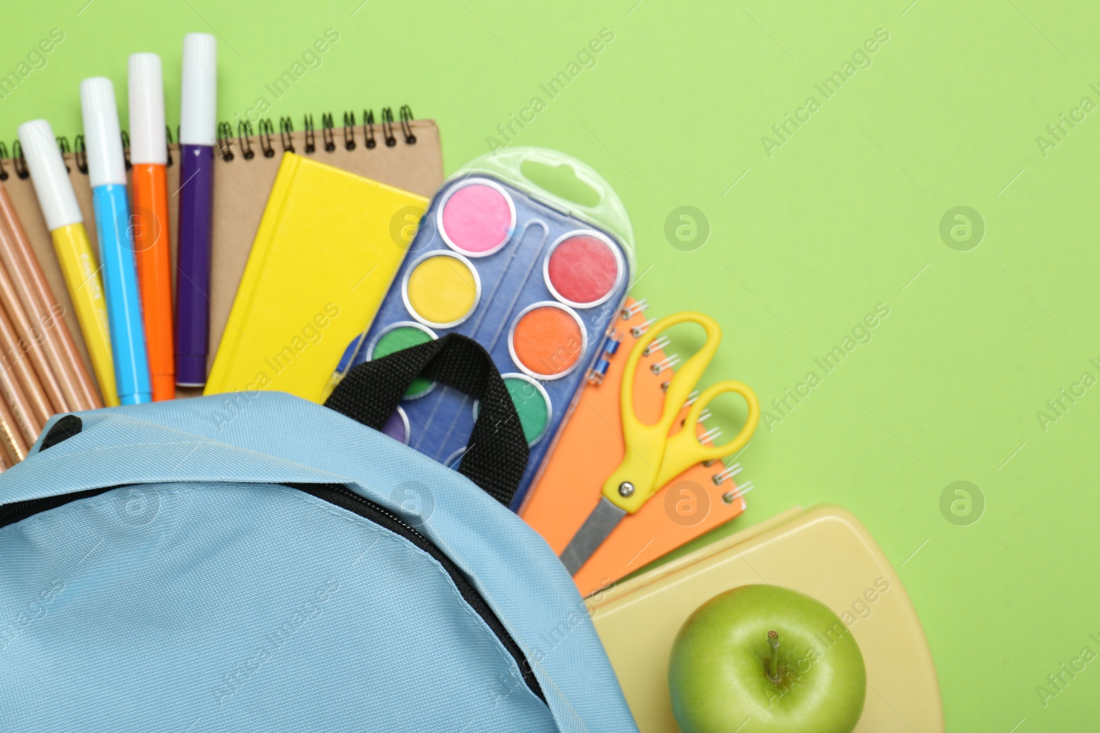 Photo of Light blue school backpack with stationery on green background, top view. Space for text