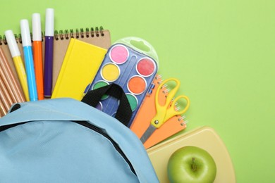 Light blue school backpack with stationery on green background, top view. Space for text