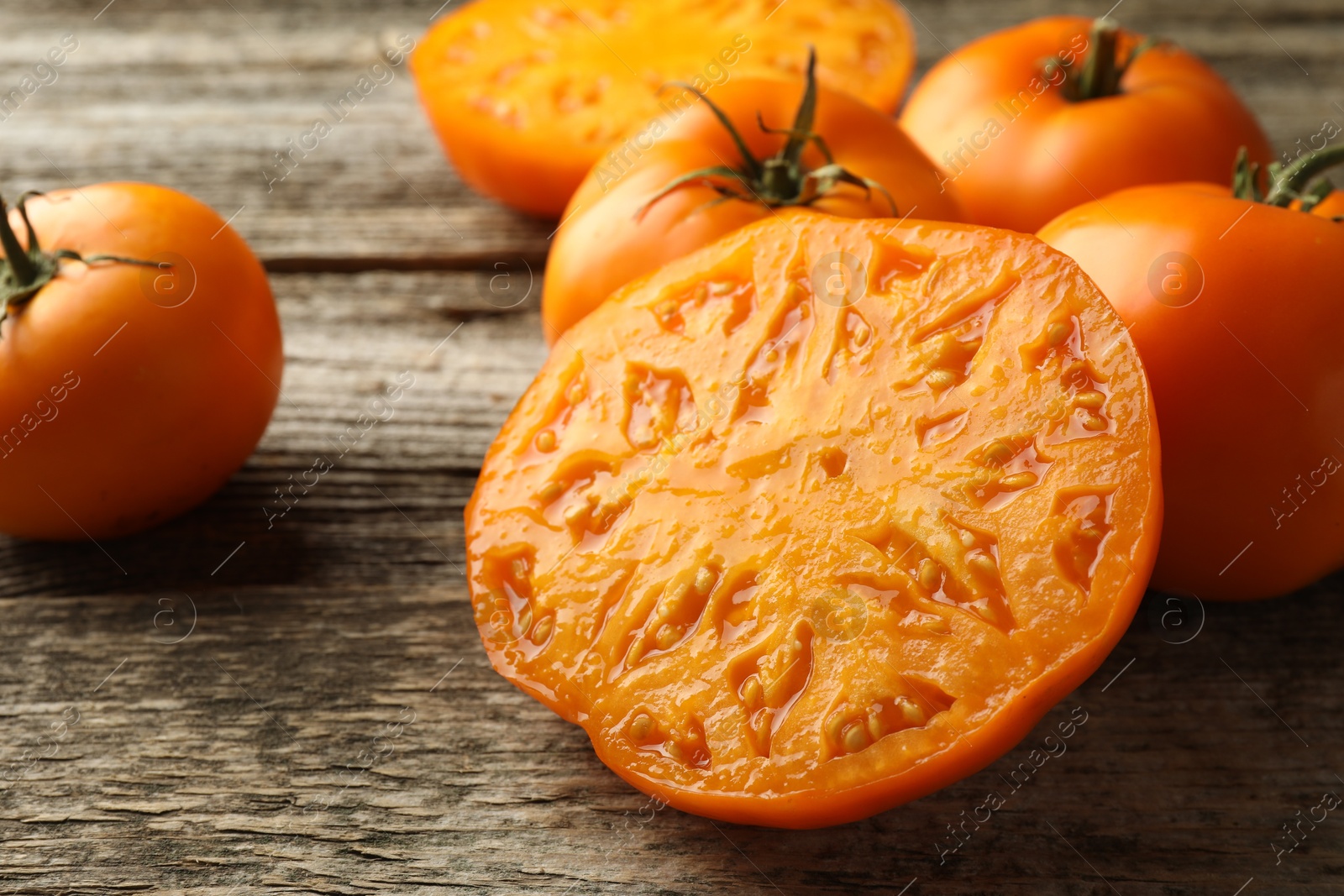 Photo of Cut and whole ripe yellow tomatoes on wooden table, closeup