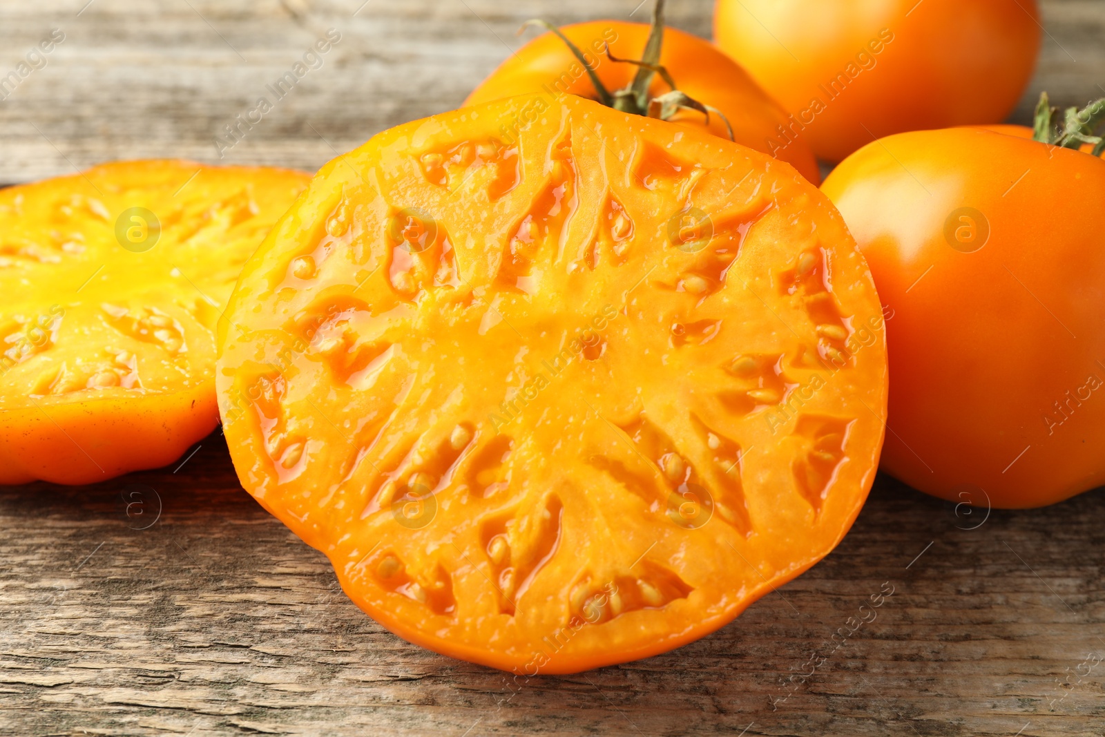 Photo of Cut and whole ripe yellow tomatoes on wooden table, closeup