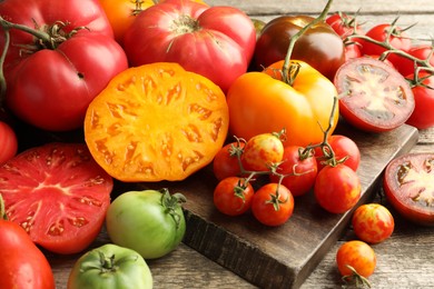 Photo of Many different ripe tomatoes on wooden table, closeup