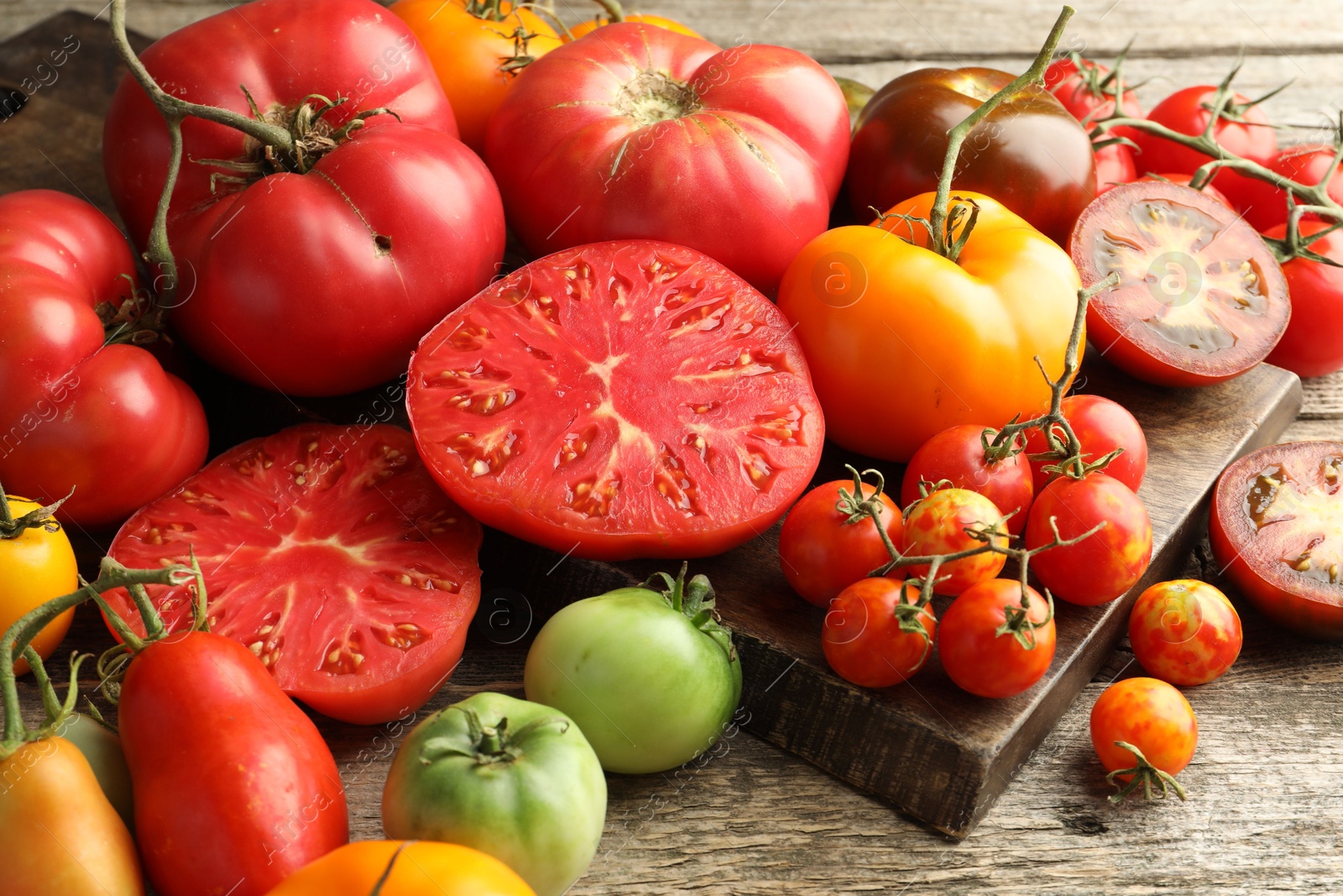 Photo of Many different ripe tomatoes on wooden table, closeup