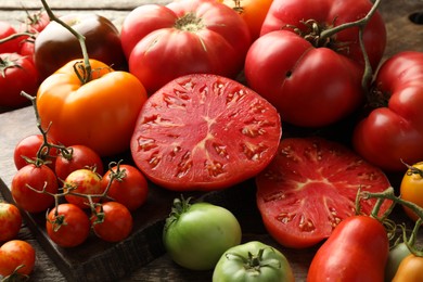 Many different ripe tomatoes on wooden table, closeup