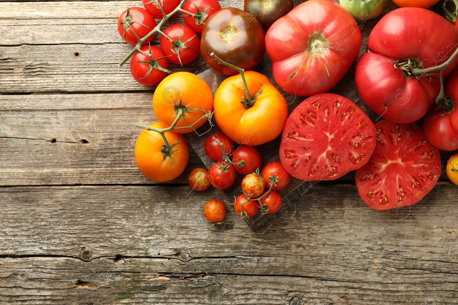 Photo of Different ripe tomatoes on wooden table, top view. Space for text