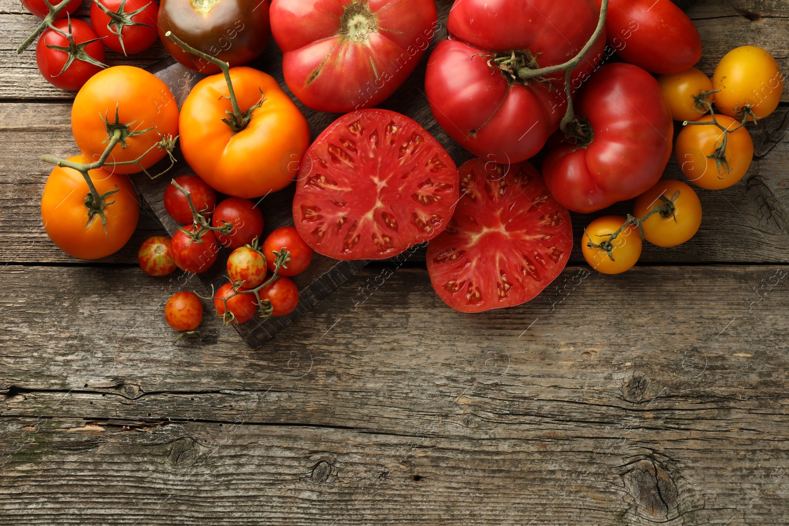 Photo of Different ripe tomatoes on wooden table, top view. Space for text