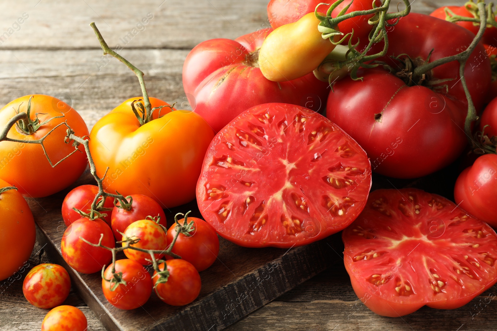 Photo of Many different ripe tomatoes on wooden table, closeup