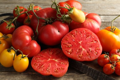 Photo of Many different ripe tomatoes on wooden table, closeup