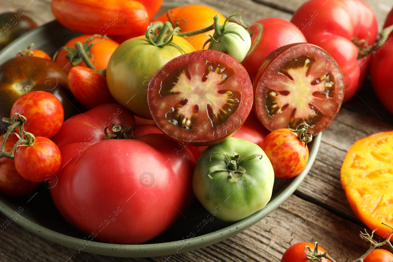 Photo of Different ripe tomatoes in bowl on wooden table, closeup