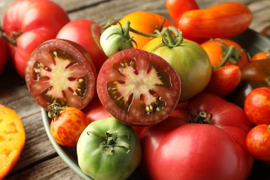 Different ripe tomatoes in bowl on wooden table, closeup