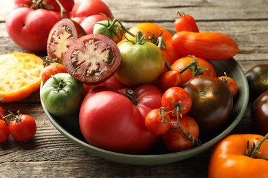 Photo of Different ripe tomatoes in bowl on wooden table, closeup