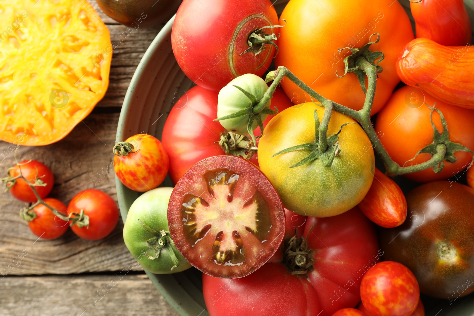 Photo of Different ripe tomatoes in bowl on wooden table, top view