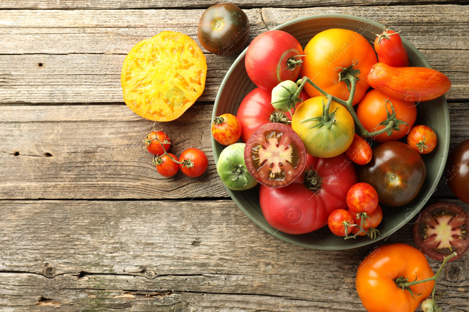 Photo of Different ripe tomatoes in bowl on wooden table, top view. Space for text