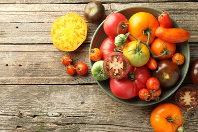 Different ripe tomatoes in bowl on wooden table, top view. Space for text