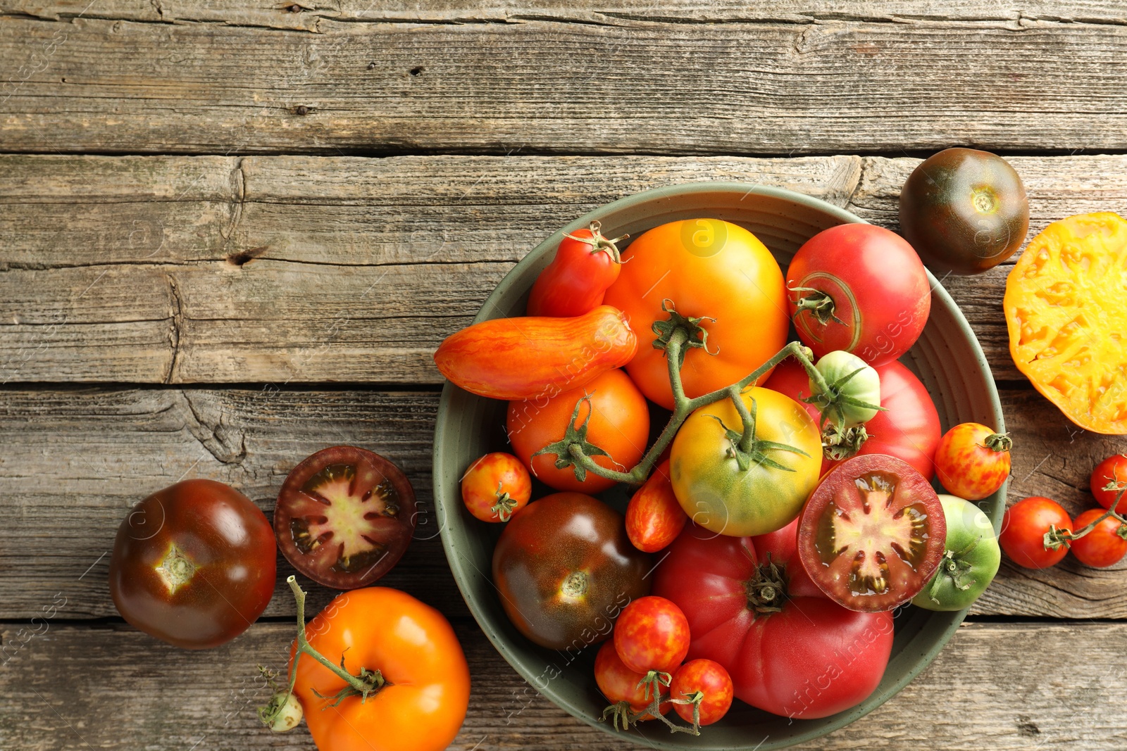 Photo of Different ripe tomatoes in bowl on wooden table, top view