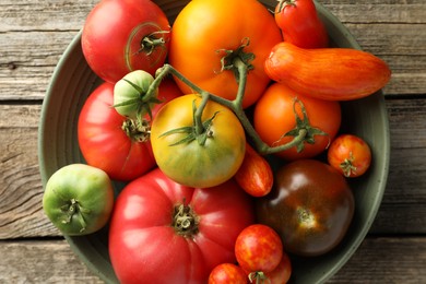 Different ripe tomatoes in bowl on wooden table, top view