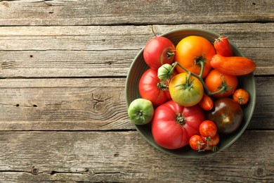 Photo of Different ripe tomatoes in bowl on wooden table, top view. Space for text