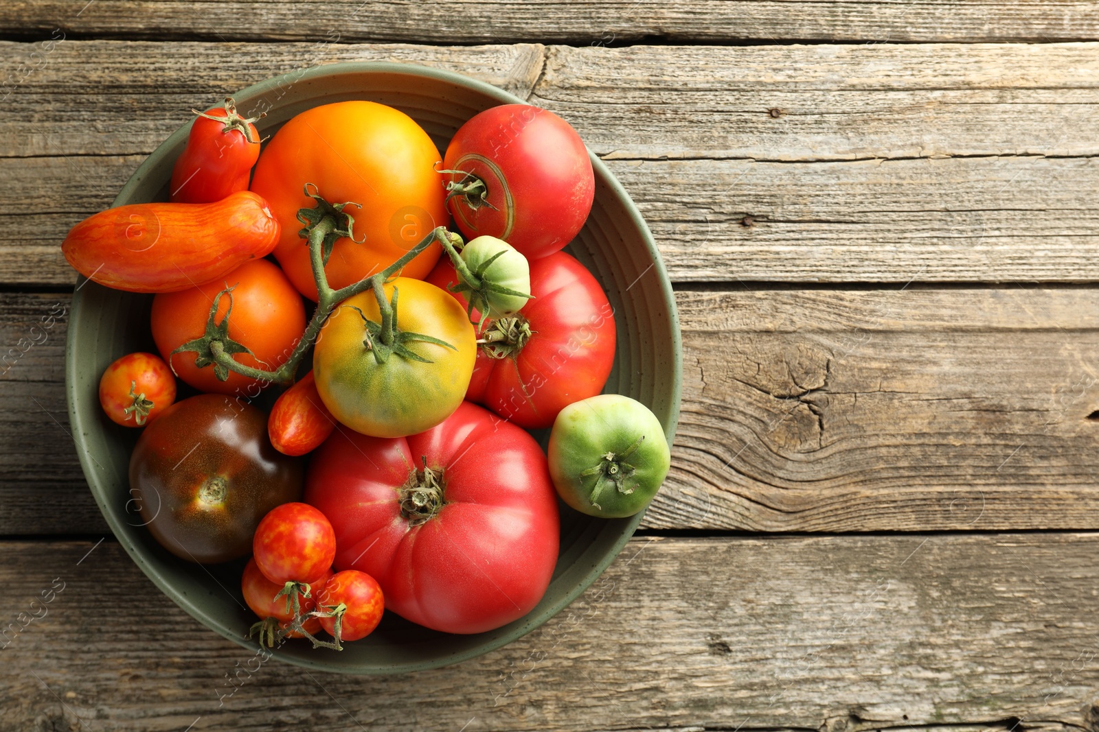 Photo of Different ripe tomatoes in bowl on wooden table, top view. Space for text