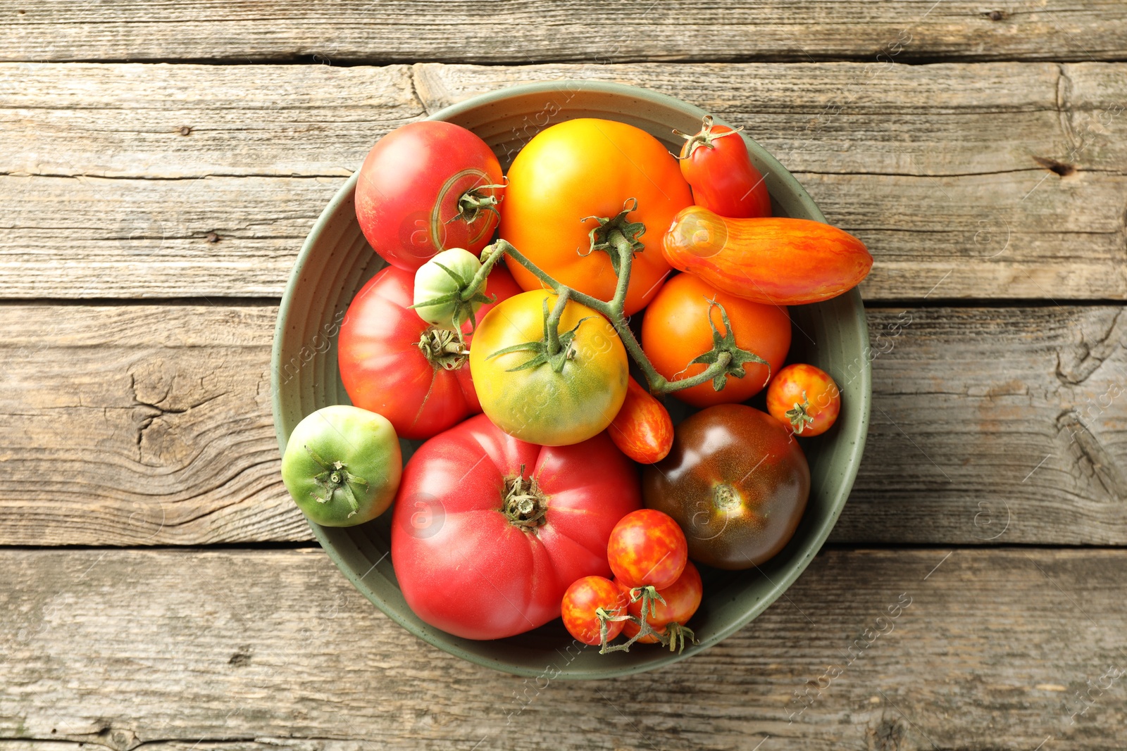 Photo of Different ripe tomatoes in bowl on wooden table, top view