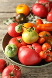 Different ripe tomatoes in bowl on wooden table, closeup