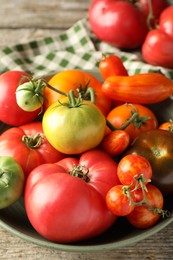 Different ripe tomatoes in bowl on wooden table, closeup